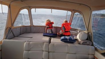 To barn i redningsvest under kalesje på båt i fart
