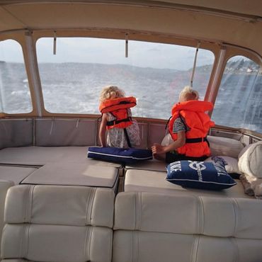 To barn i redningsvest under kalesje på båt i fart